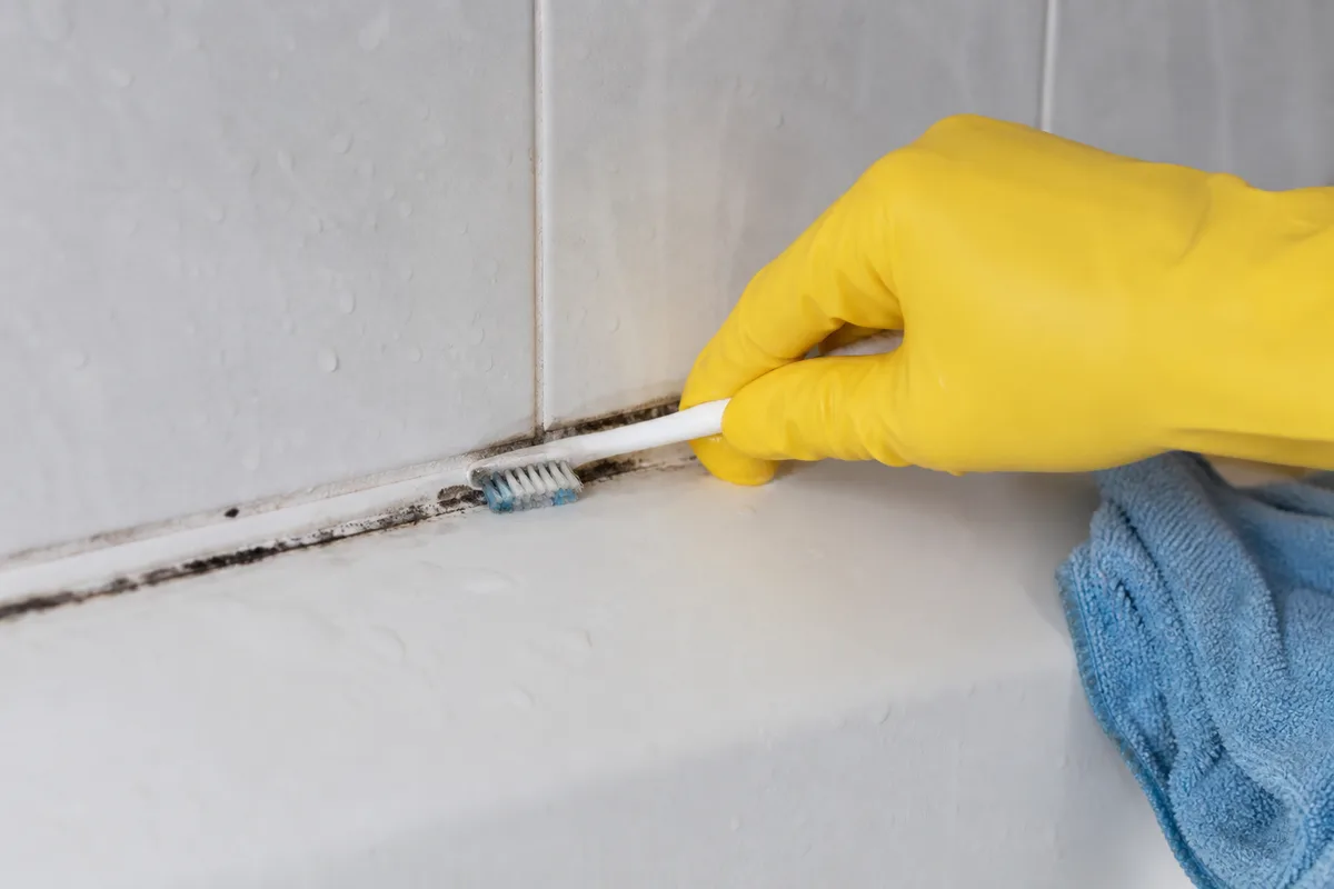 Main gantée nettoyant un joint de silicone noirci au bord d&rsquo;une baignoire