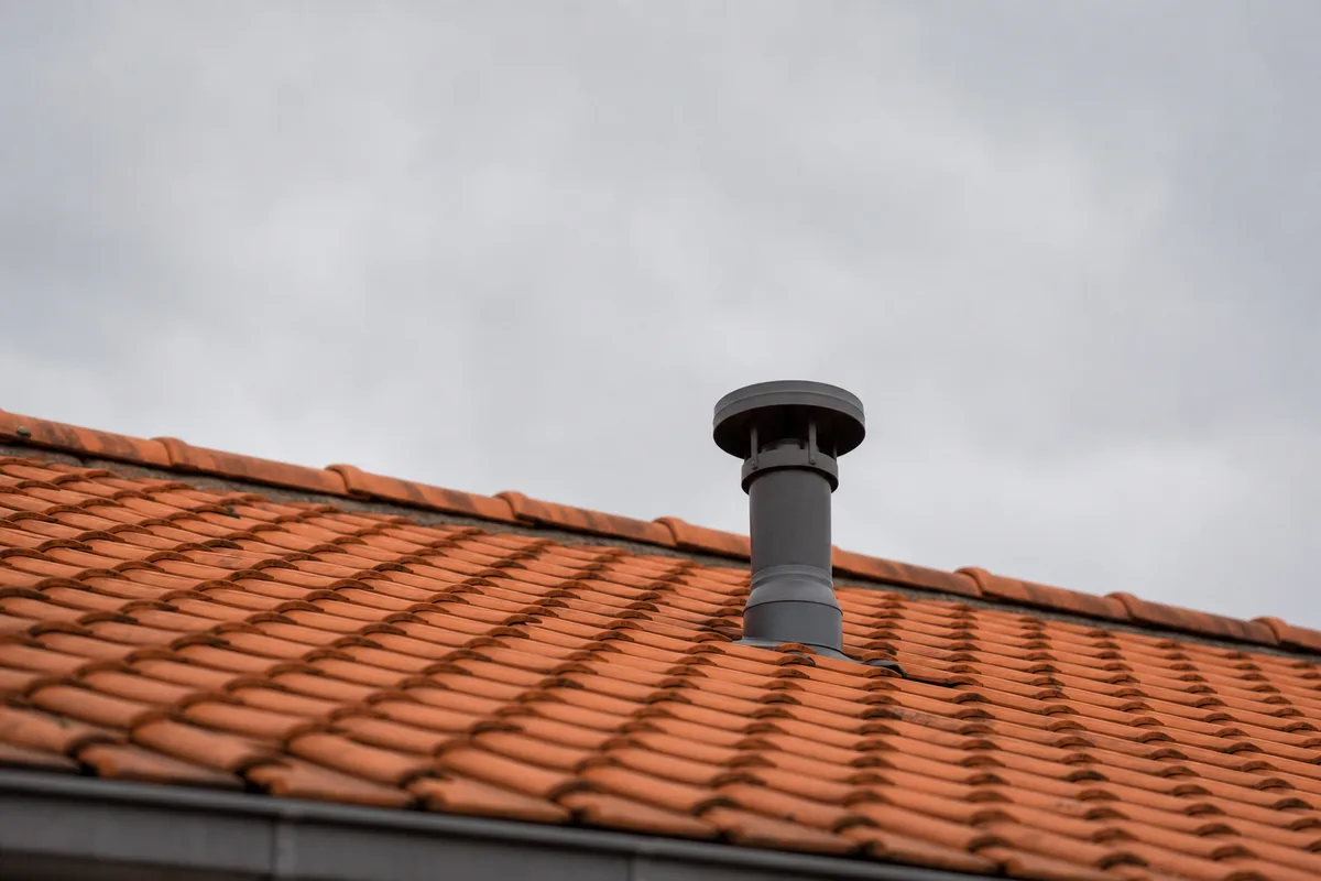 Sortie de ventilation en toiture sur un toit de tuiles rouges sous un ciel gris